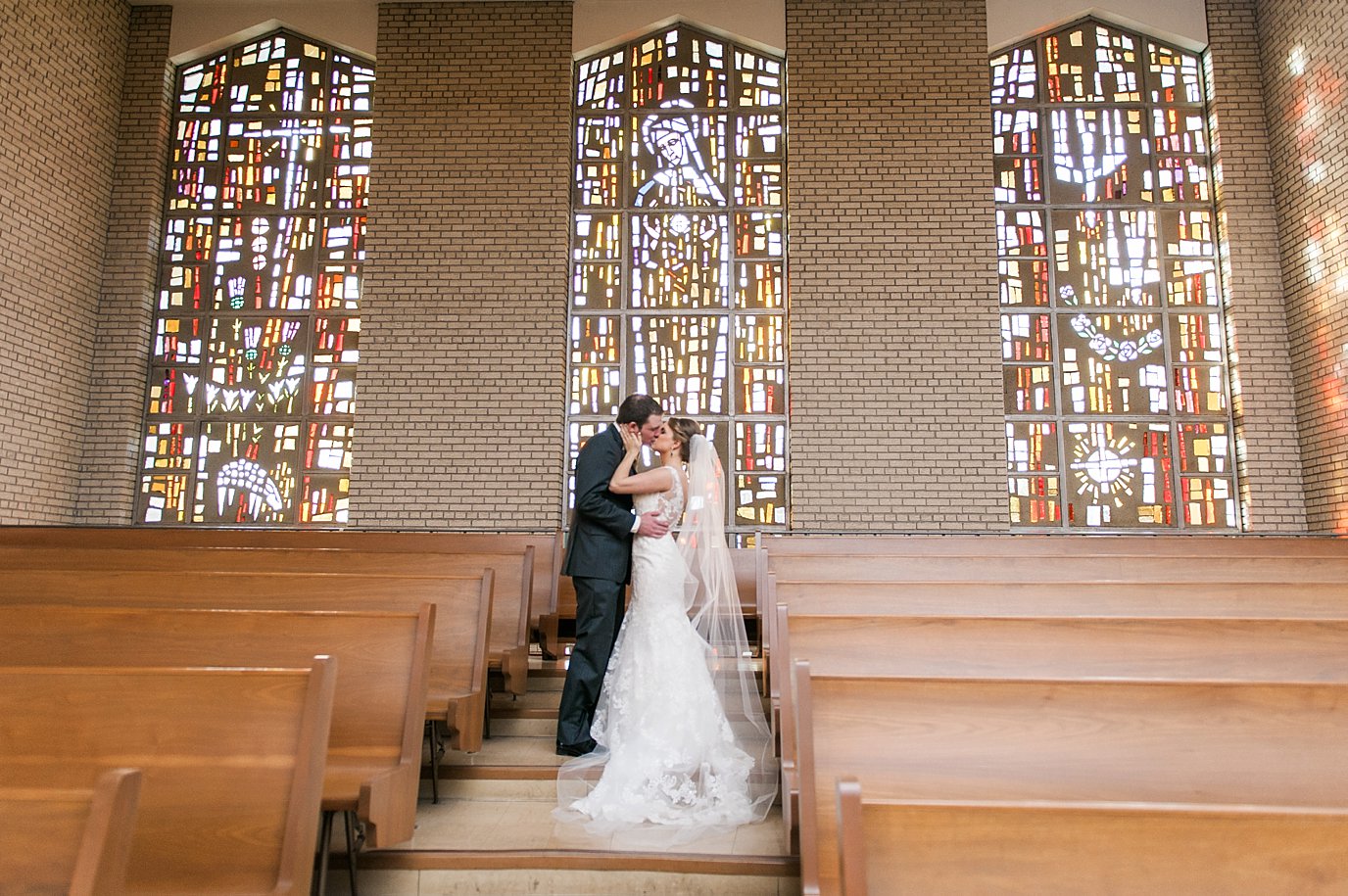 bride and groom kiss near stain glass windows
